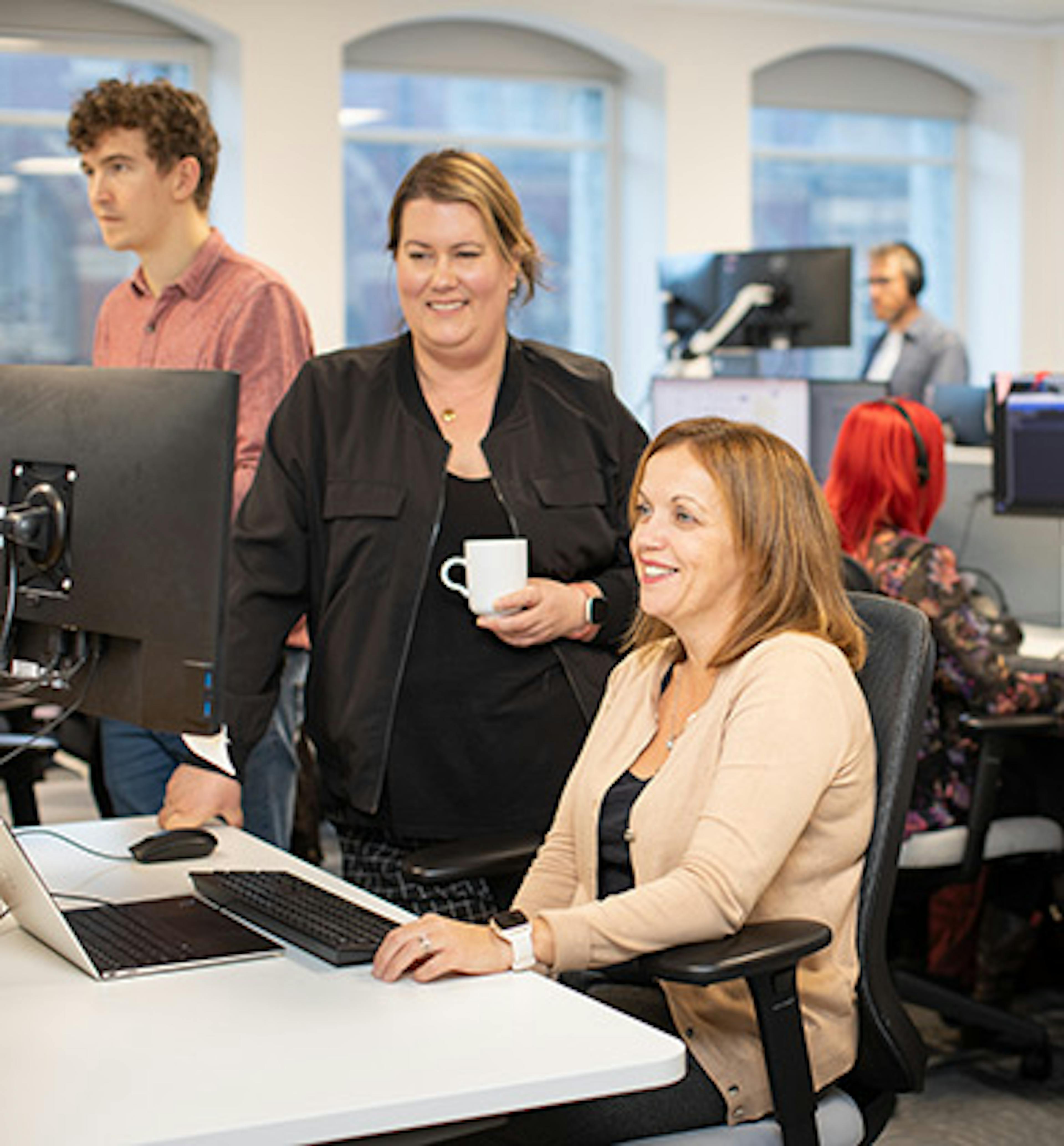 People working in an office, with two women in the left foreground looking at a computer screen