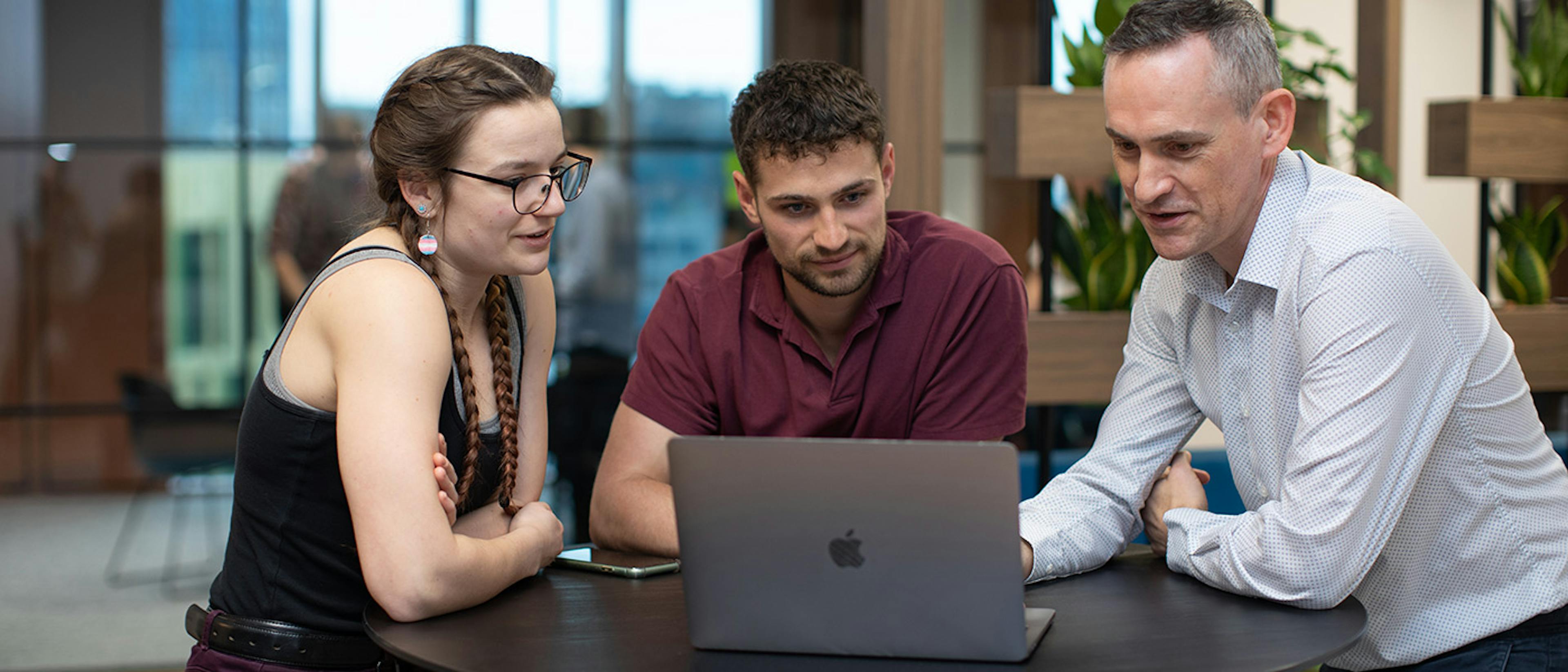 Three people in a stand-up meeting looking at a laptop screen