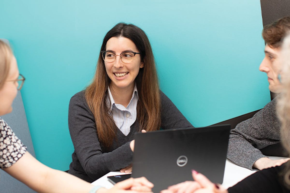 Four employees sat around a desk with a laptop