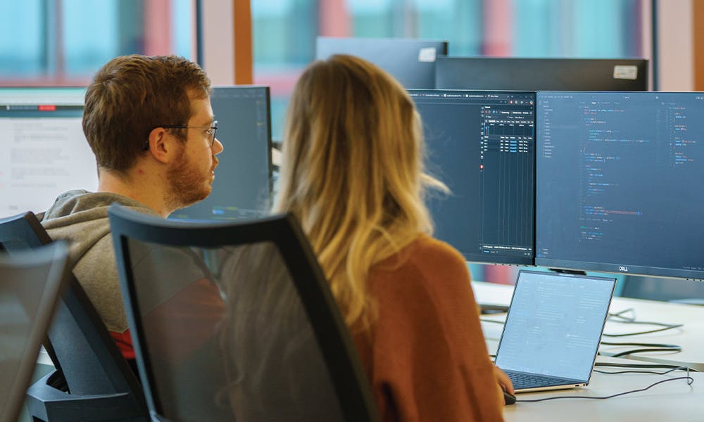 Person sat at a desk behind a computer monitor with code on it