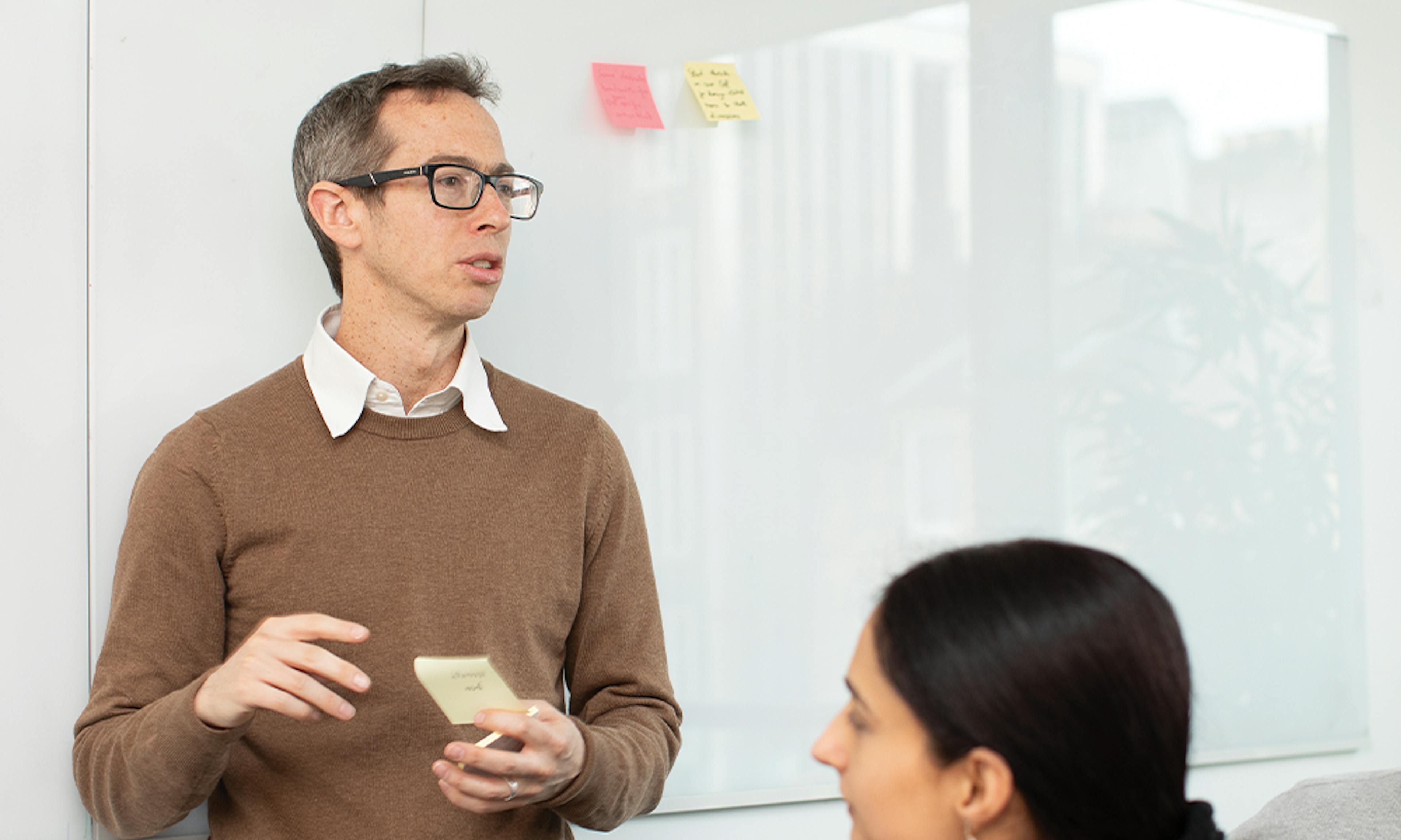 Person stands in front of white board with sticky notes addressing others