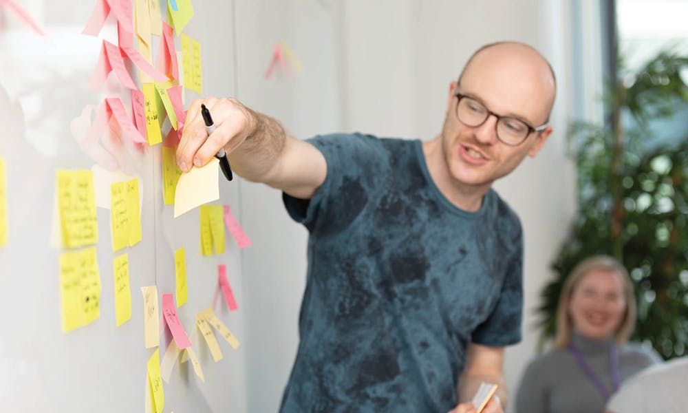 Man in a meeting adding a sticky note to a white board