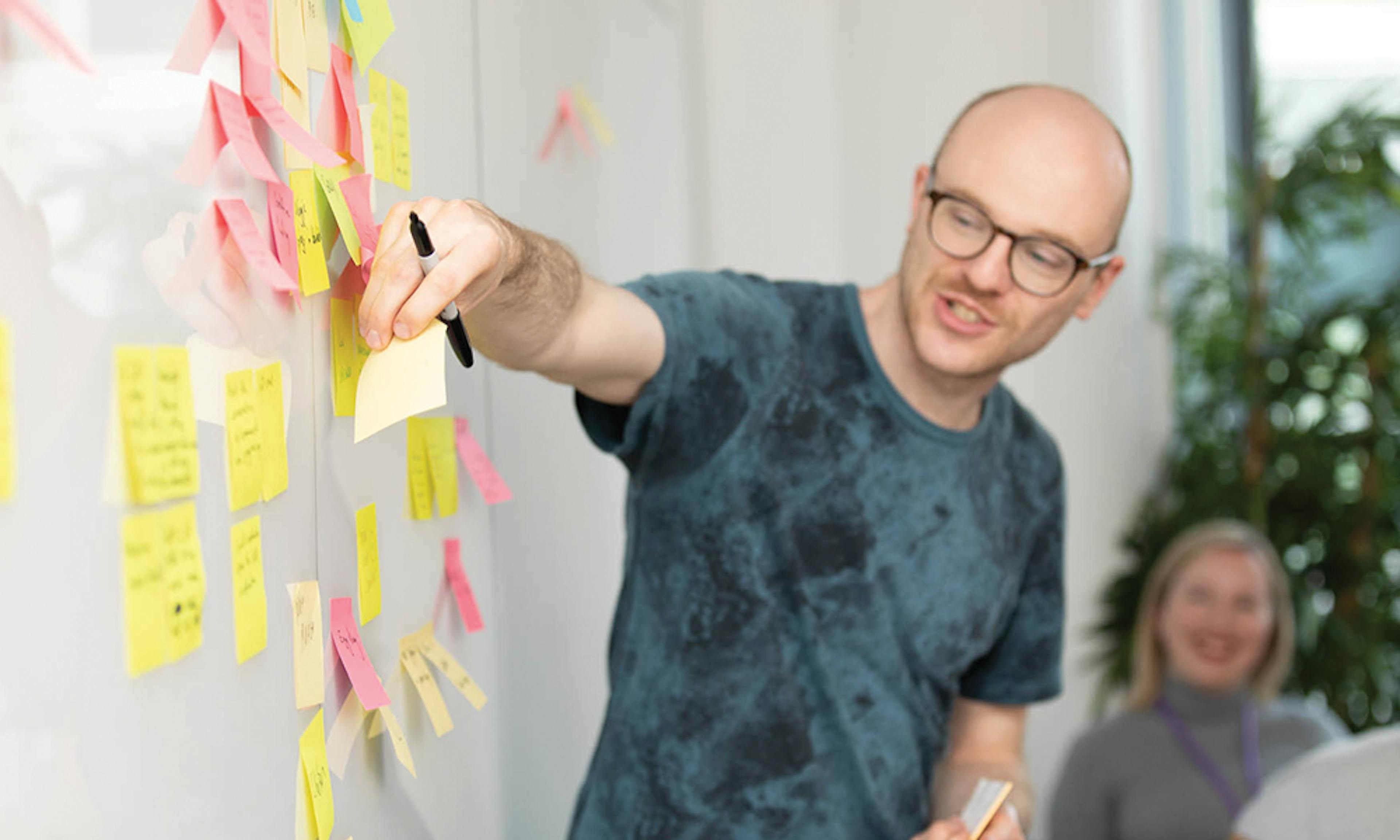 Man in a meeting adding a sticky note to a white board