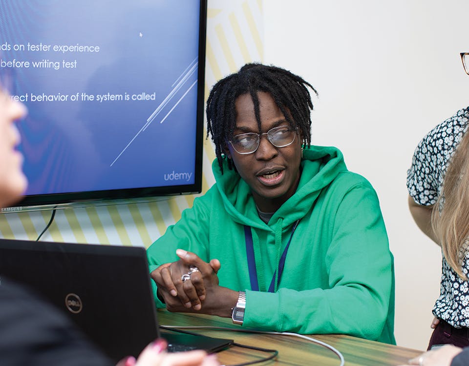 Meeting around laptop with large screen on the wall behind
