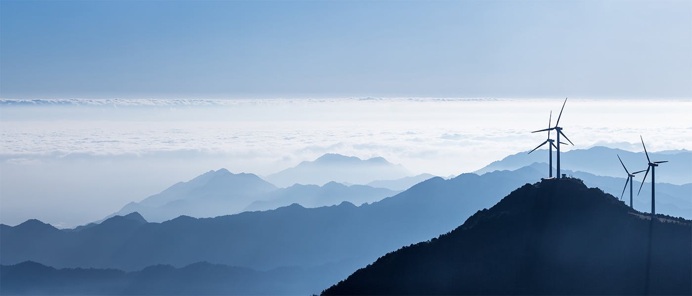 Mountain peaks above the clouds on a sunny day with wind turbines on the nearest peak