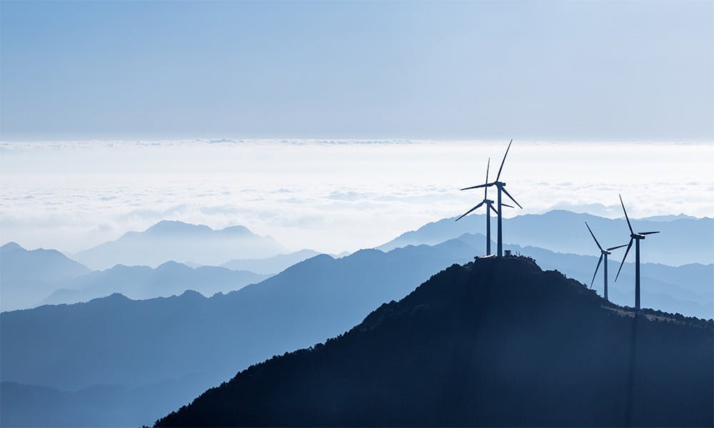 Mountain peaks above the clouds on a sunny day with wind turbines on the nearest peak