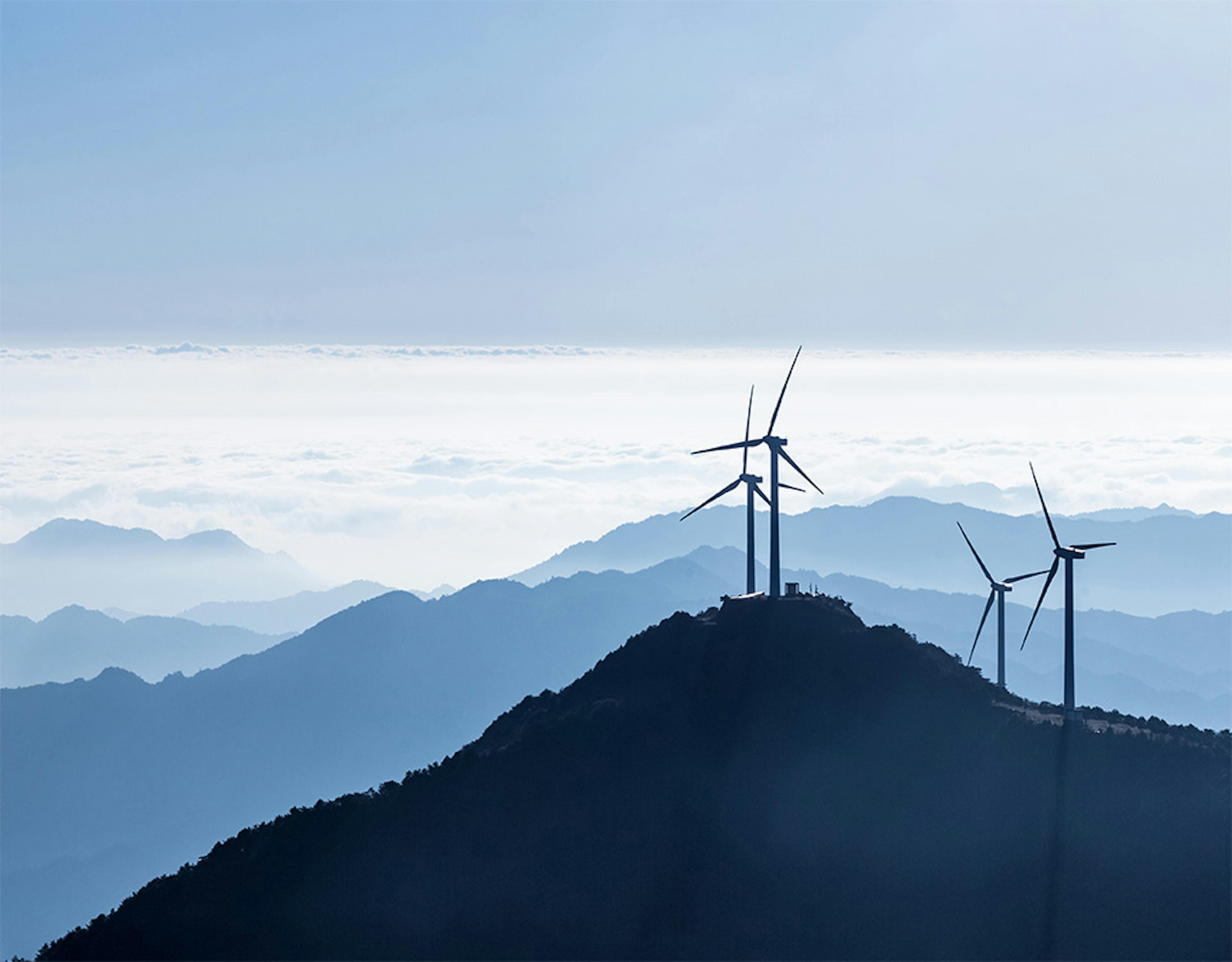 Mountain peaks above the clouds on a sunny day with wind turbines on the nearest peak