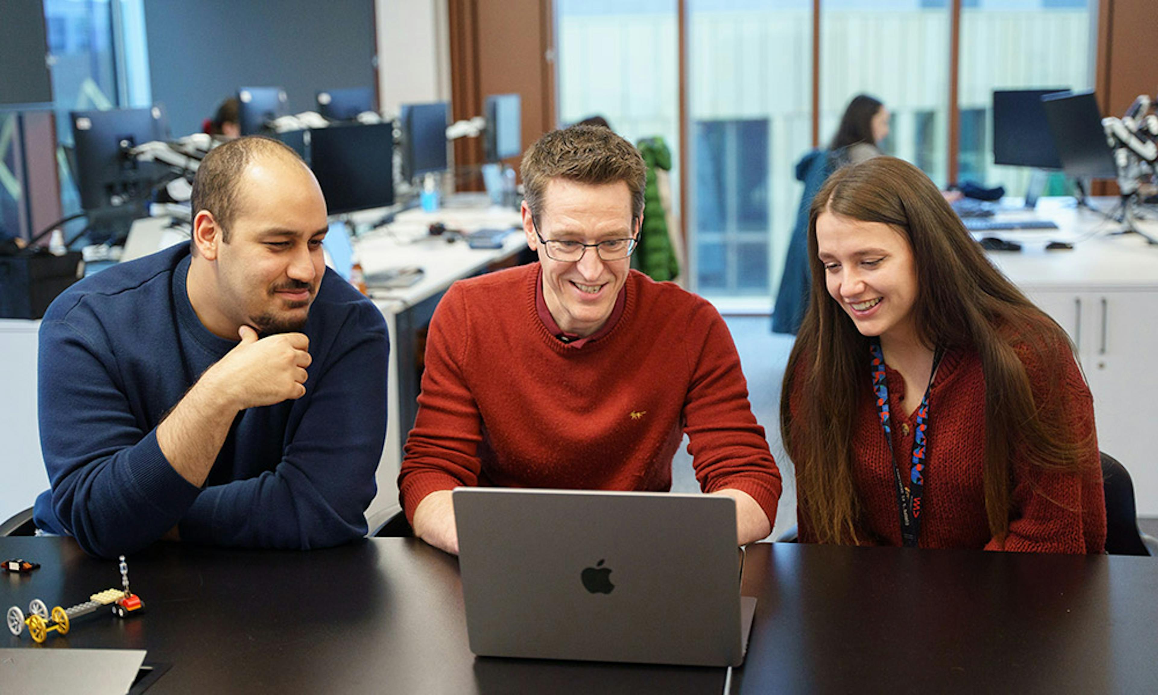 Three people looking at a computer screen in an office setting