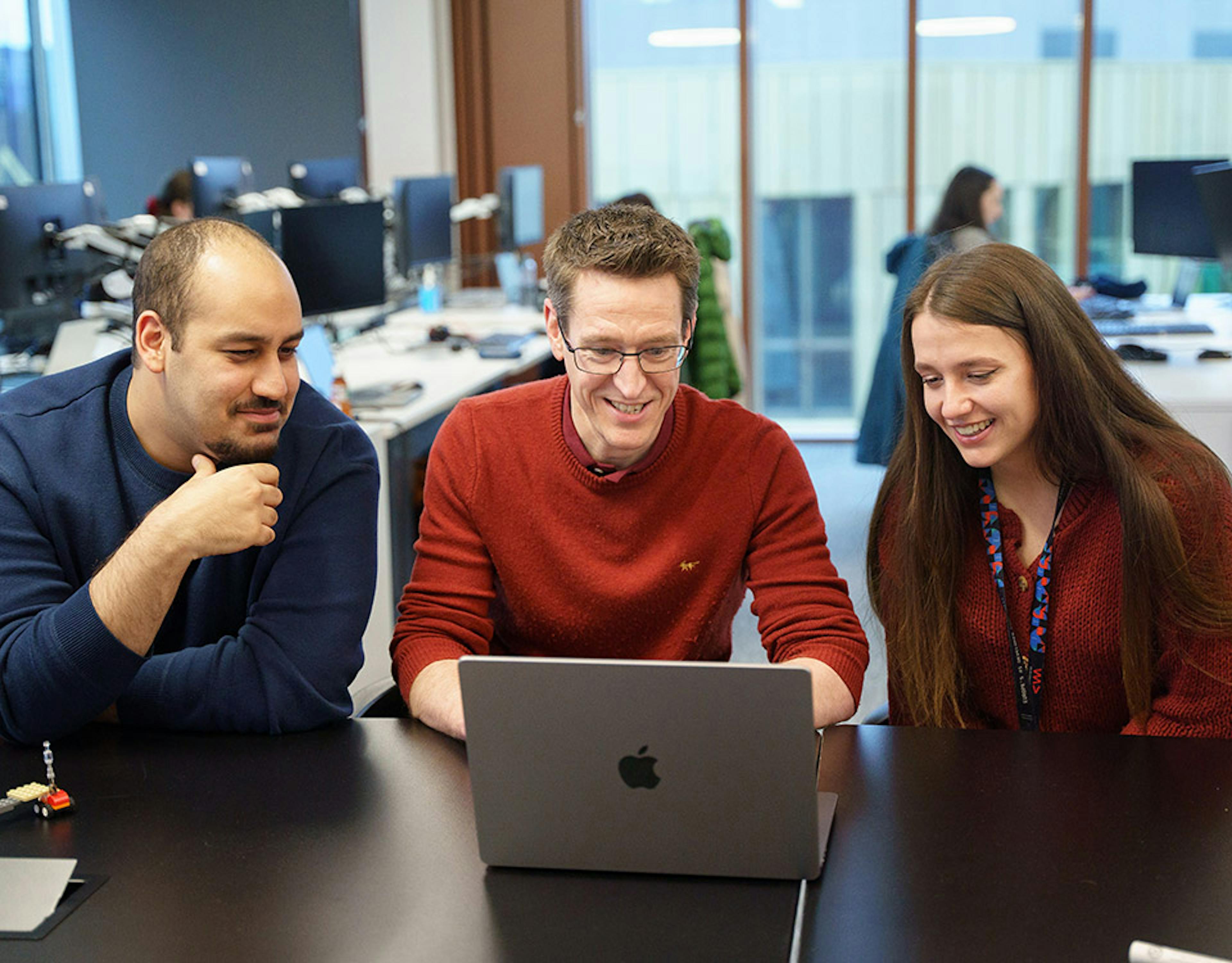 Three people looking at a computer screen in an office setting