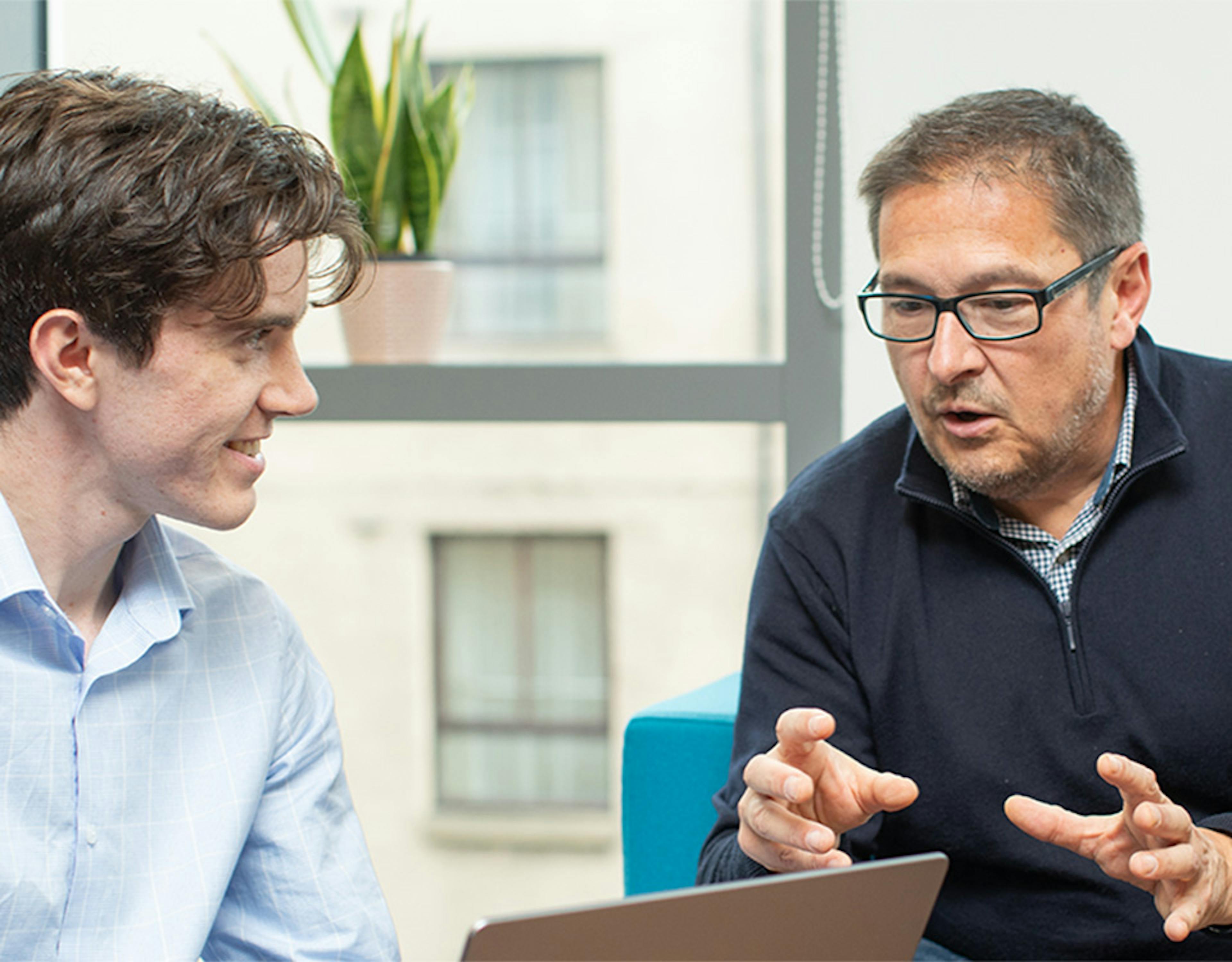 Three people in an informal meeting, with the person on the left holding a laptop