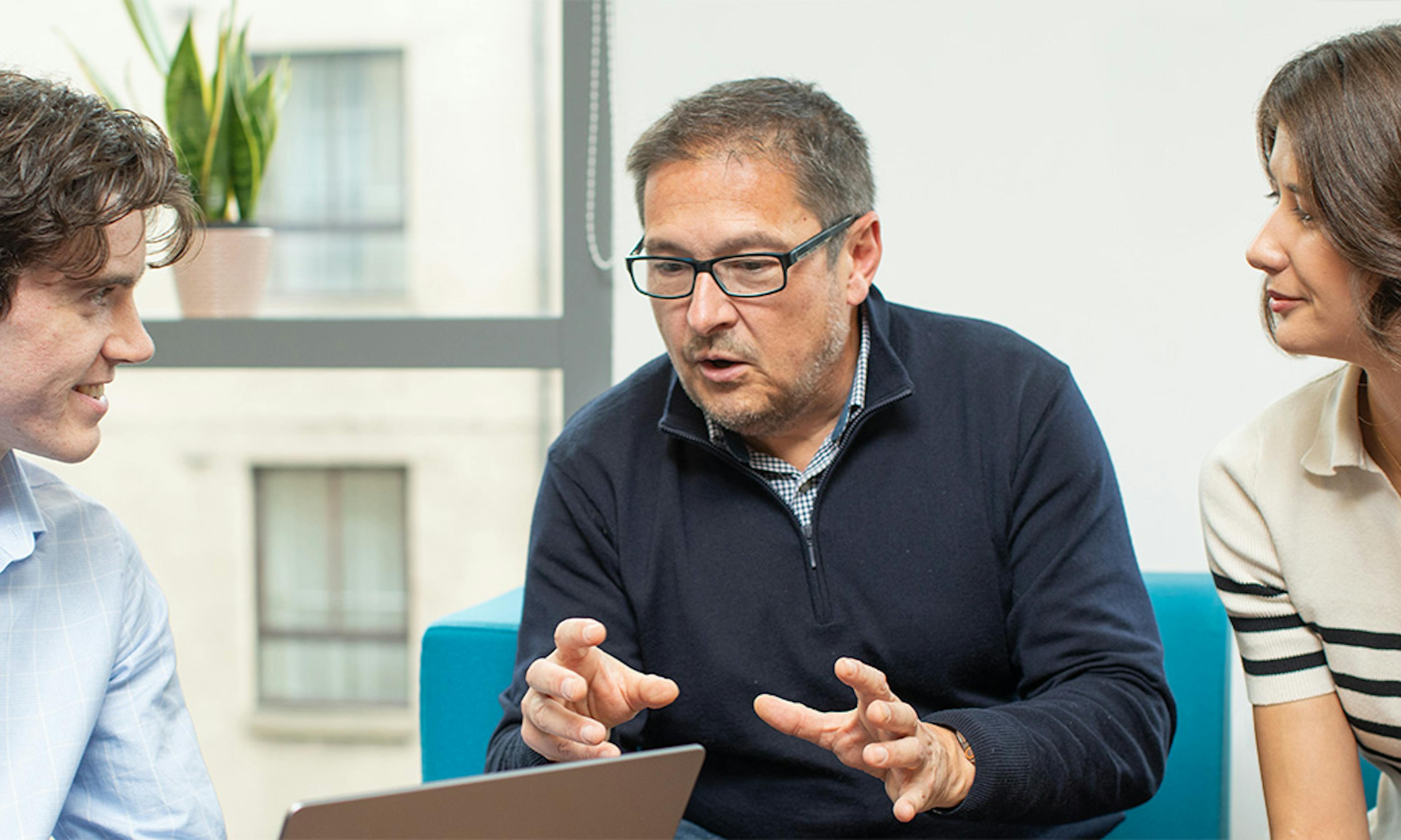 Three people in an informal meeting, with the person on the left holding a laptop