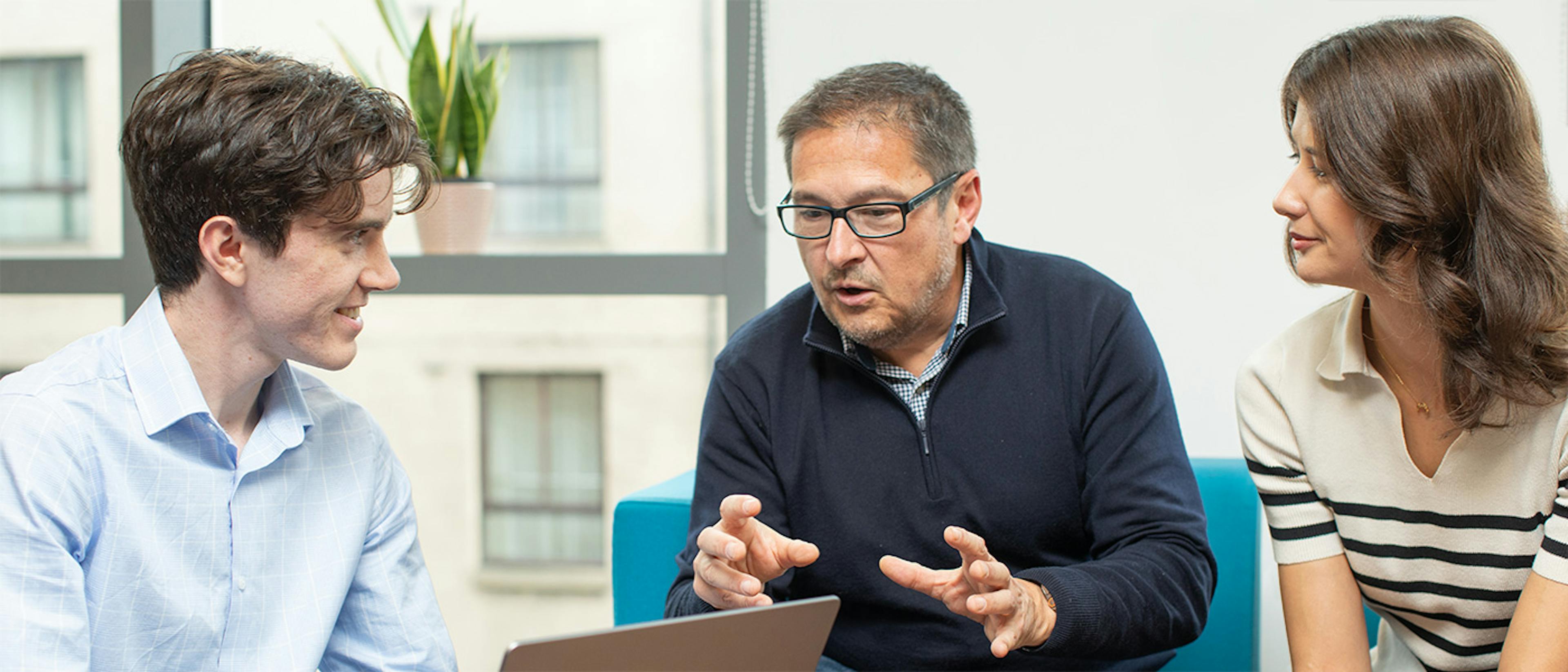 Three people in an informal meeting, with the person on the left holding a laptop