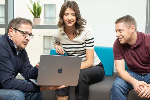 Three people in an informal meeting, discussing something on a laptop screen