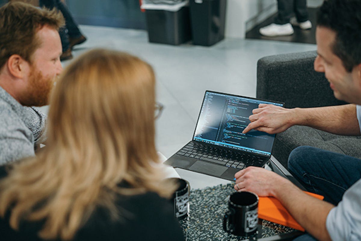 Three people in an informal meeting discussing some code on a laptop screen