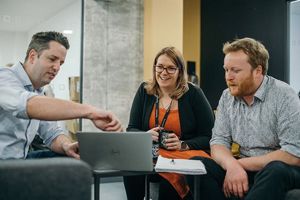 Three people in an informal meeting discussing something on a laptop screen