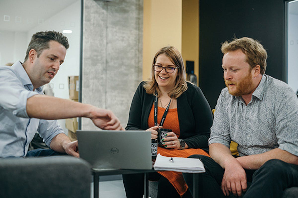 Three people in an informal meeting discussing something on a laptop screen