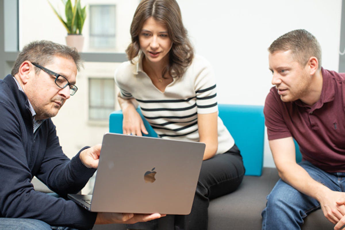 Three people in an informal meeting are looking at something on a laptop screen
