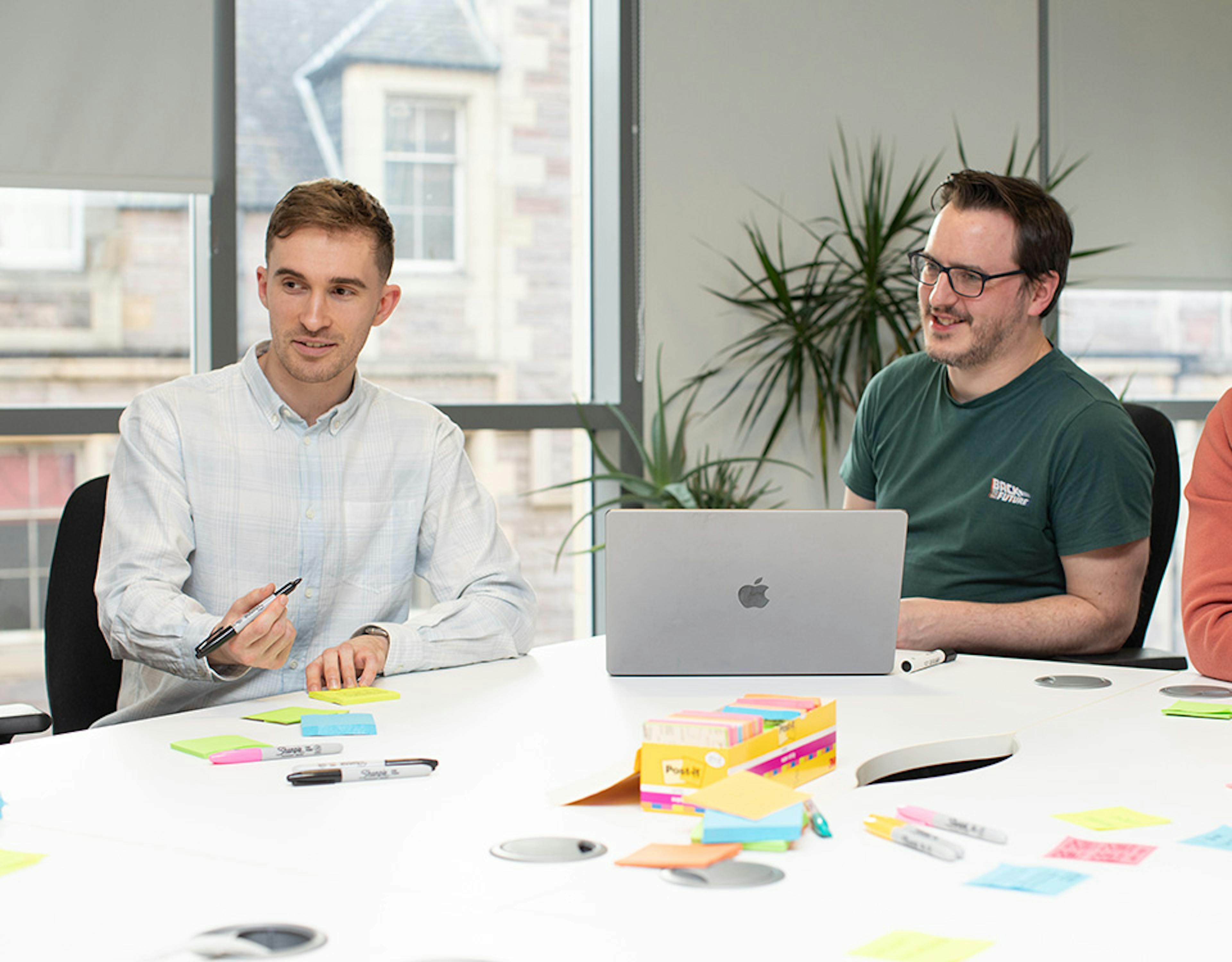 Three UX designers in a meeting around a big table with a laptop and sticky notes