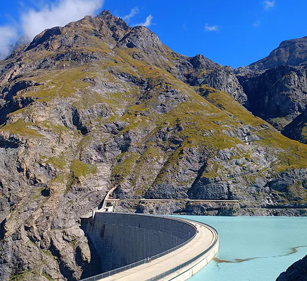 A dam in the curving around in the foreground with Mauvoisin Reservoir on the right and a mountain in the background