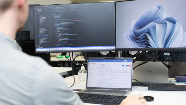 Person coding with three screens in an office setting