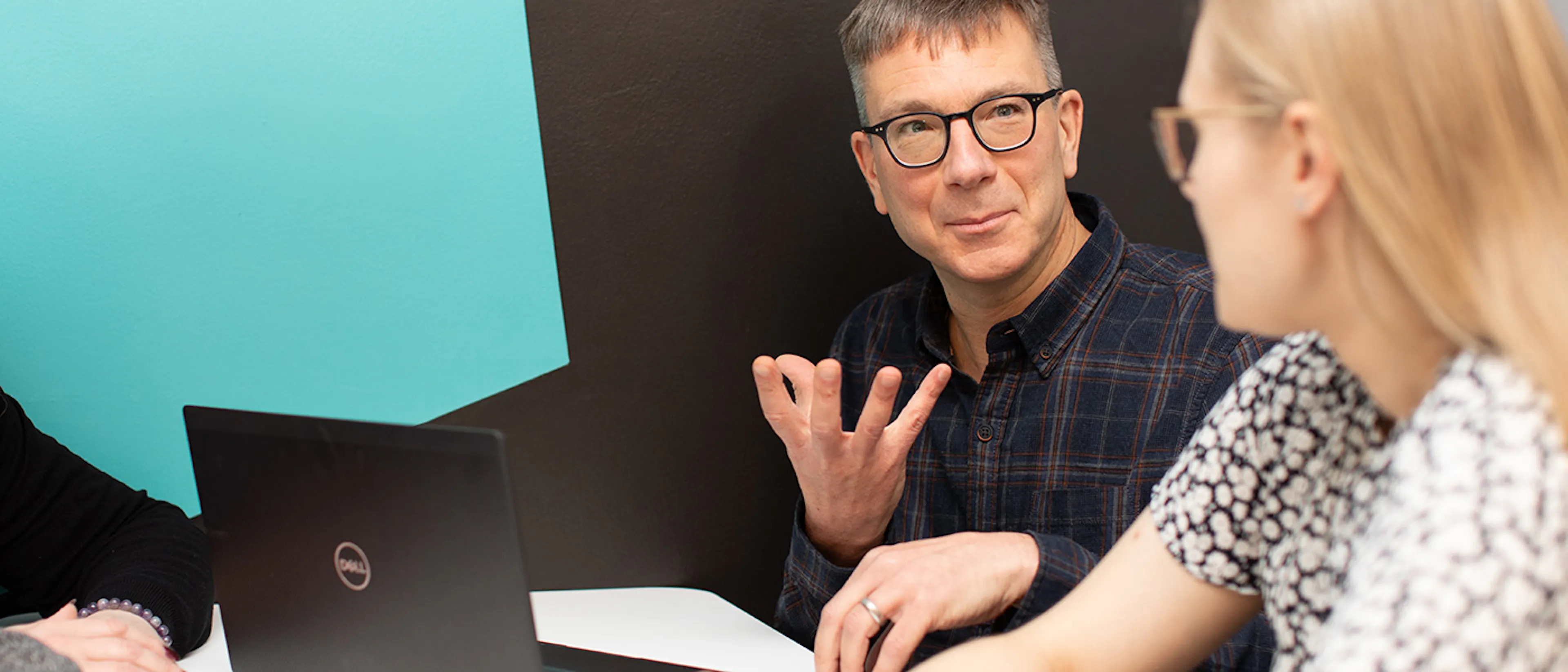 A person with a laptop talking to another person in a meeting setting