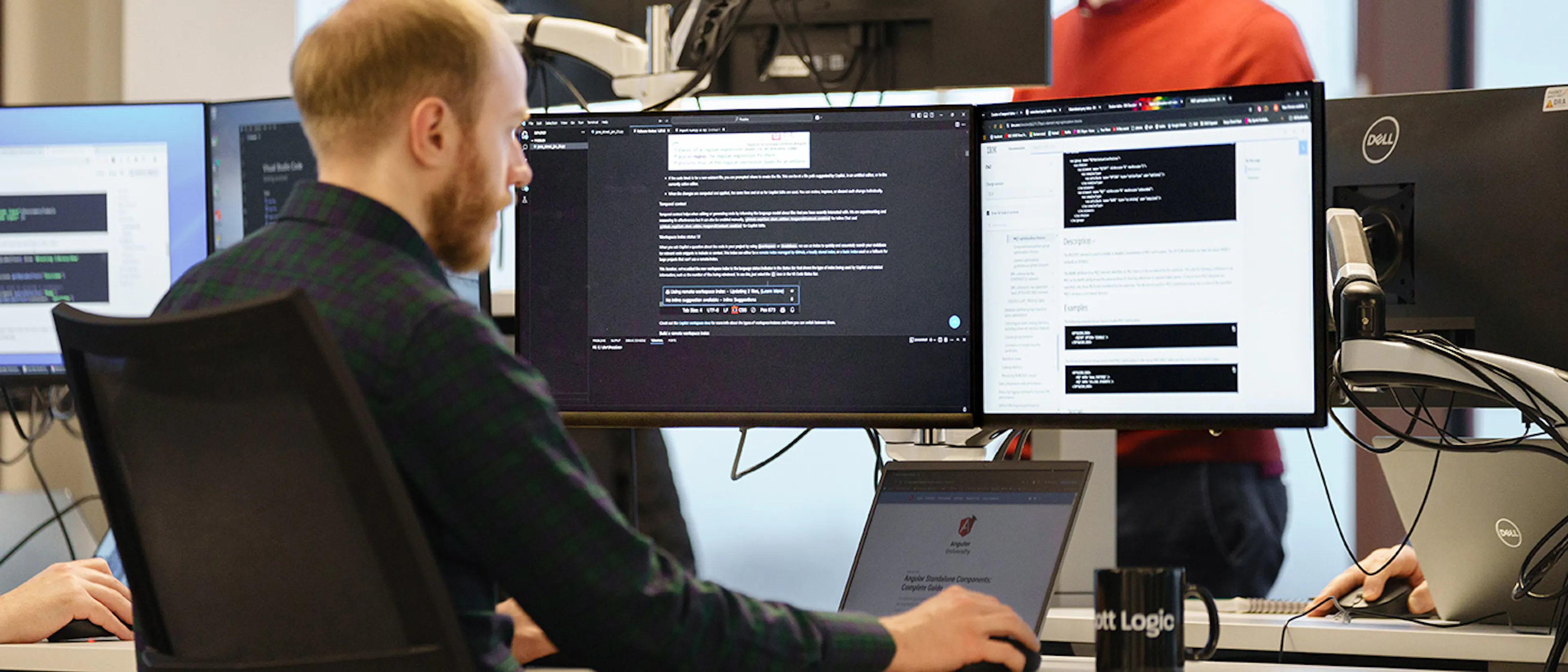 A developer in an office setting, working with three screens