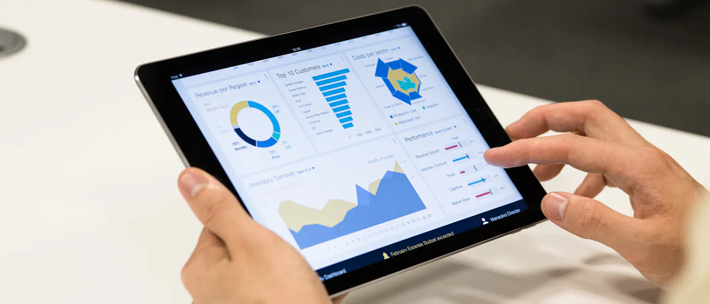 A person holding a tablet computer displaying a dashboard of charts