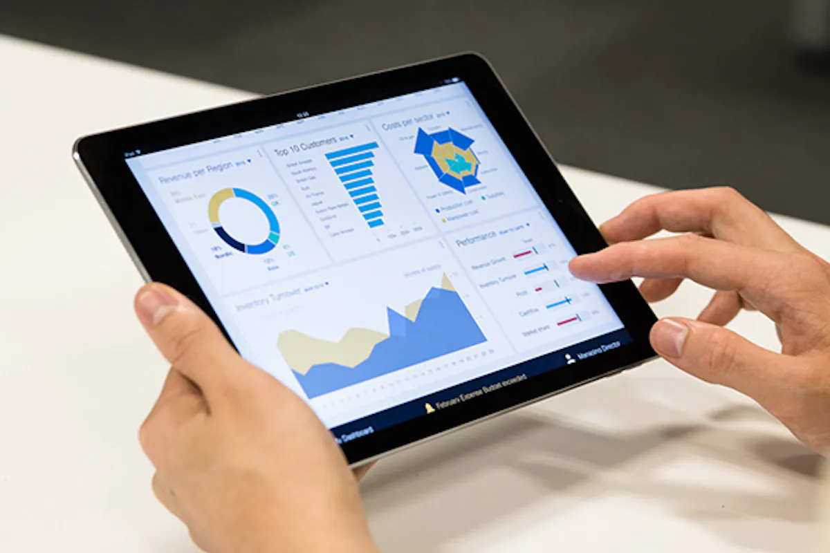 A person holding a tablet computer displaying a dashboard of charts