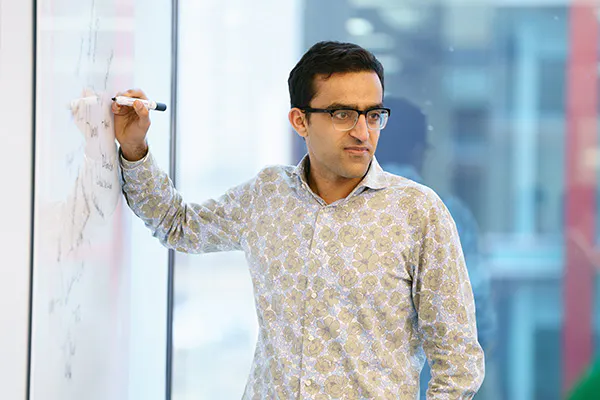 A person in an office setting, writing on a whiteboard