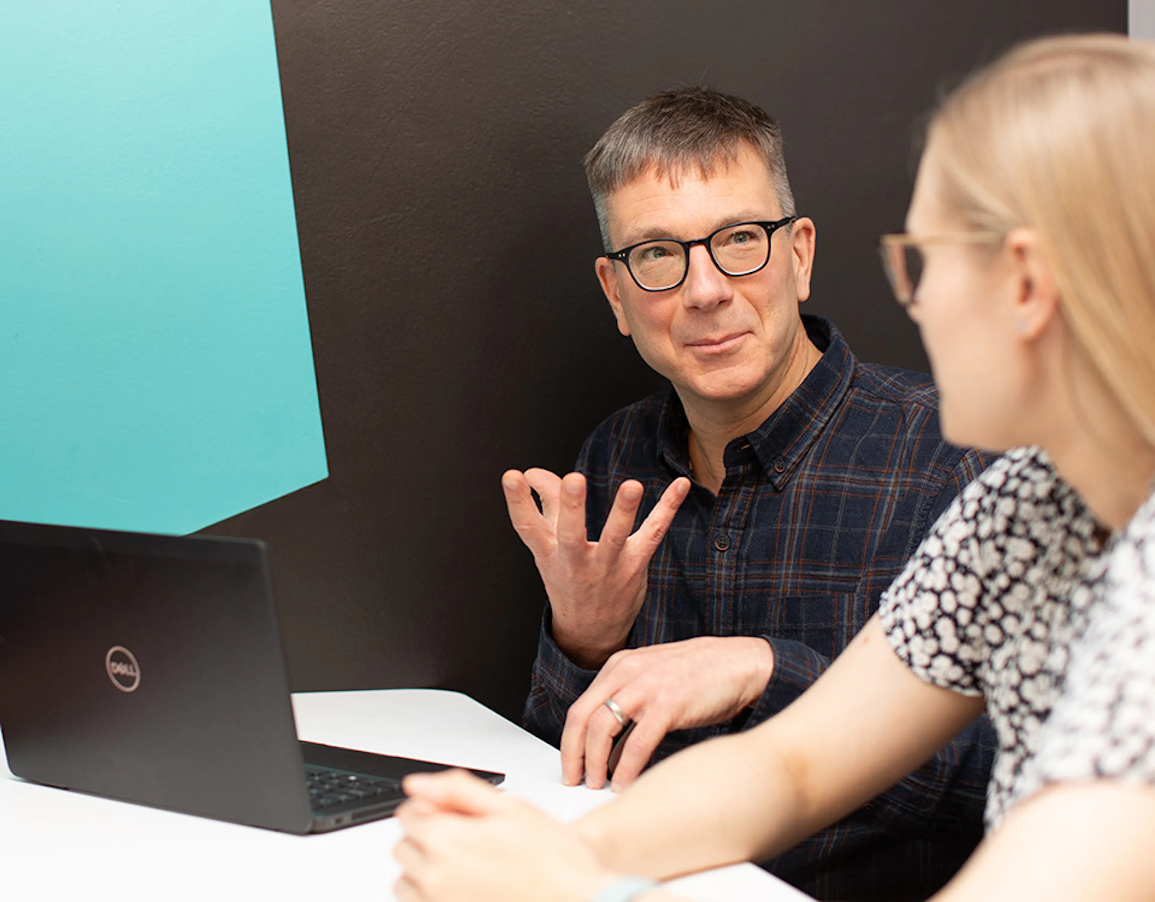 A person with a laptop talking to another person in a meeting setting