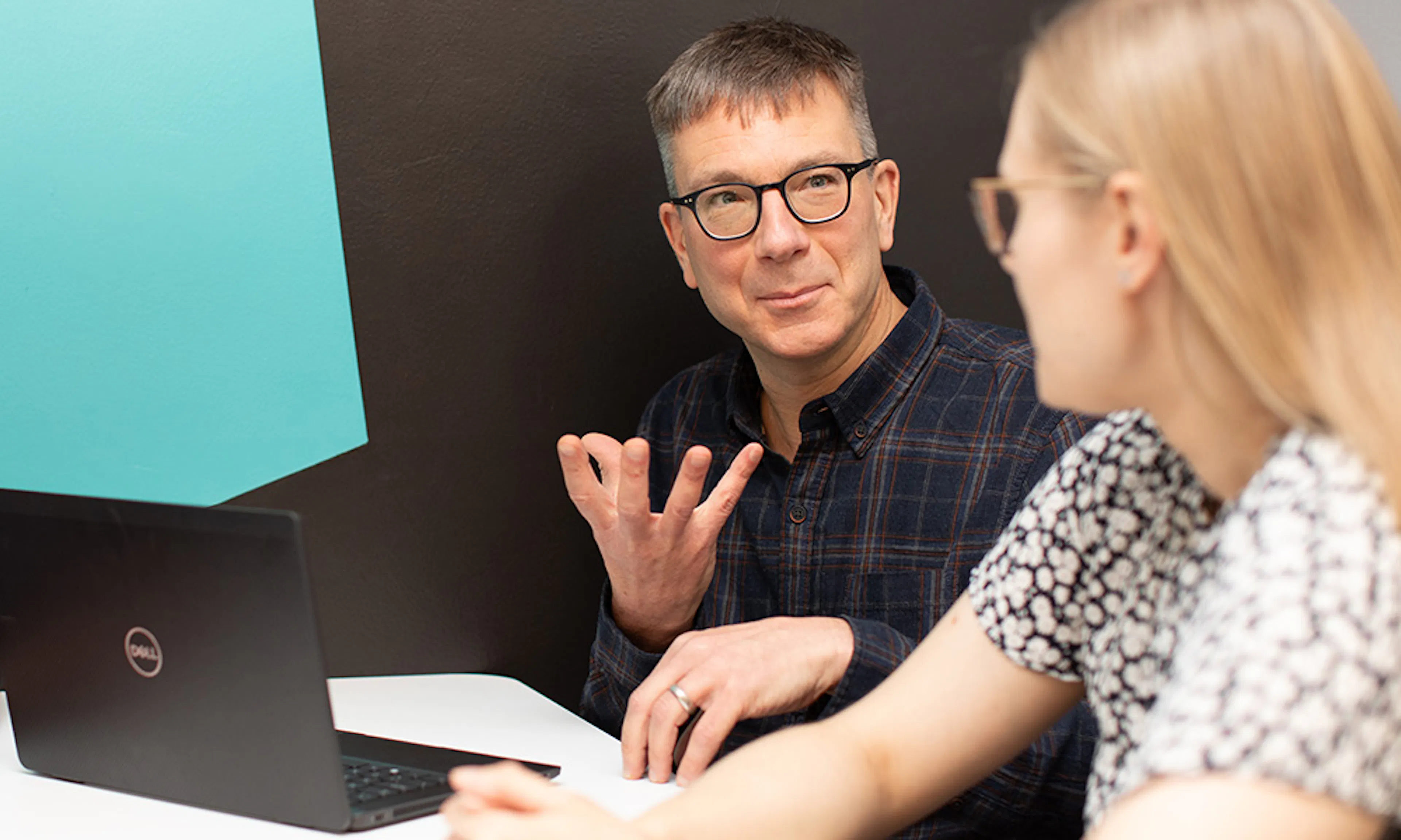 A person with a laptop talking to another person in a meeting setting