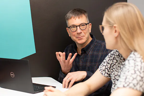 A person with a laptop talking to another person in a meeting setting