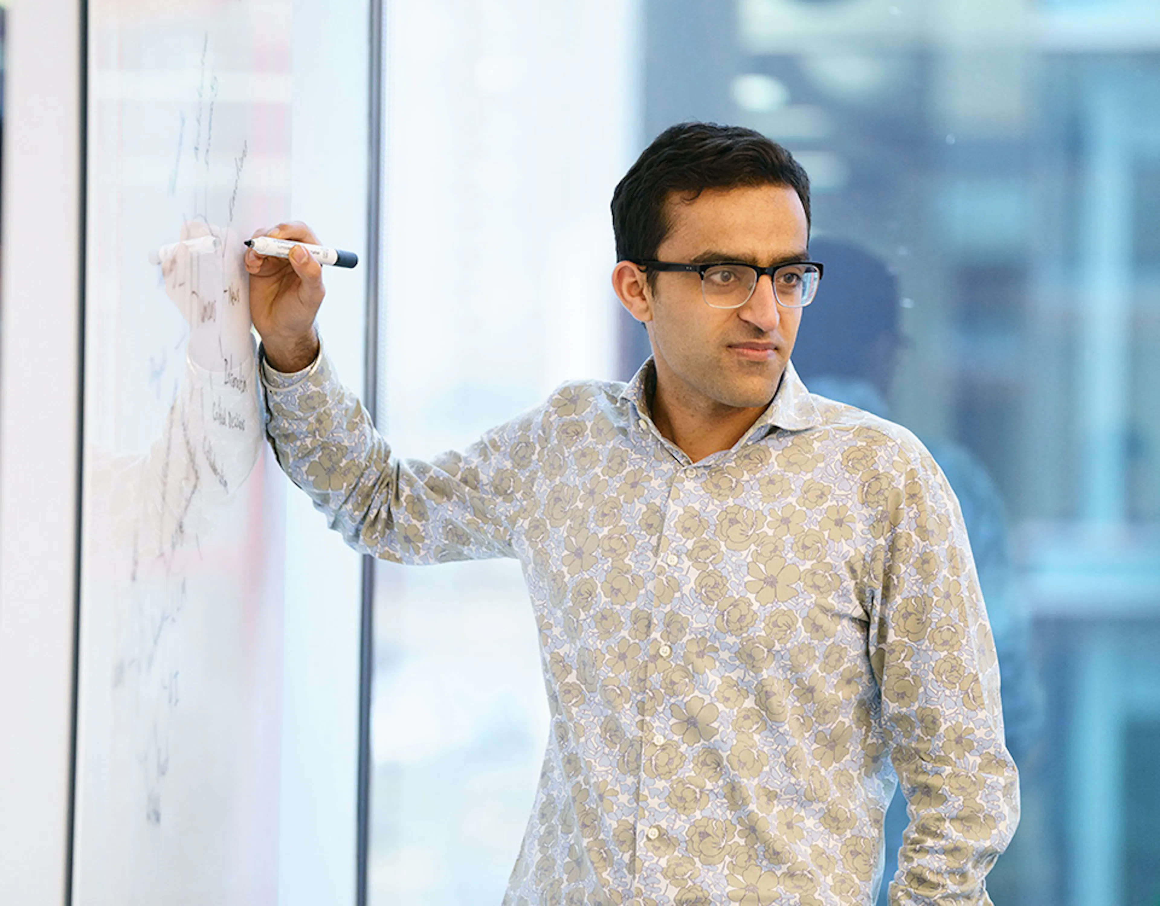 A person in an office setting, writing on a whiteboard