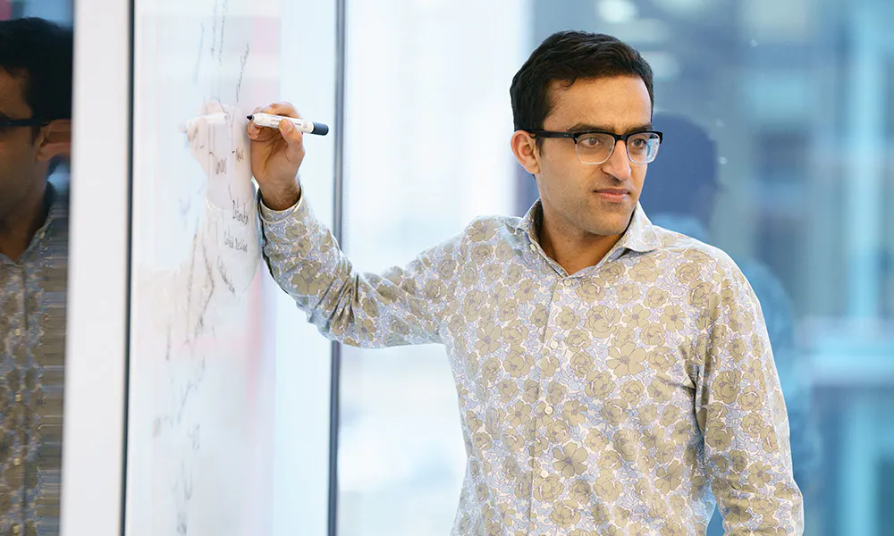 A person in an office setting, writing on a whiteboard