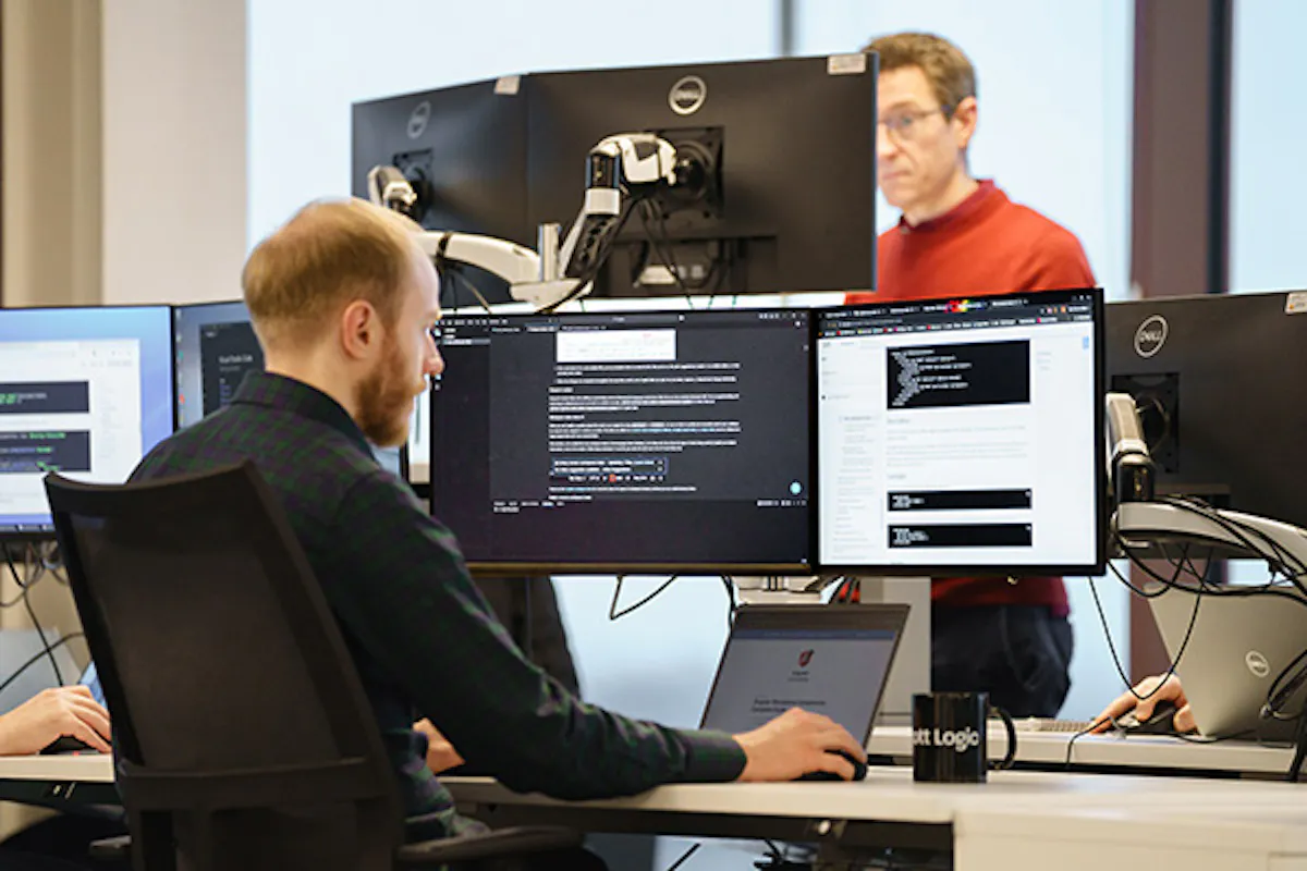 A developer in an office setting, working with three screens