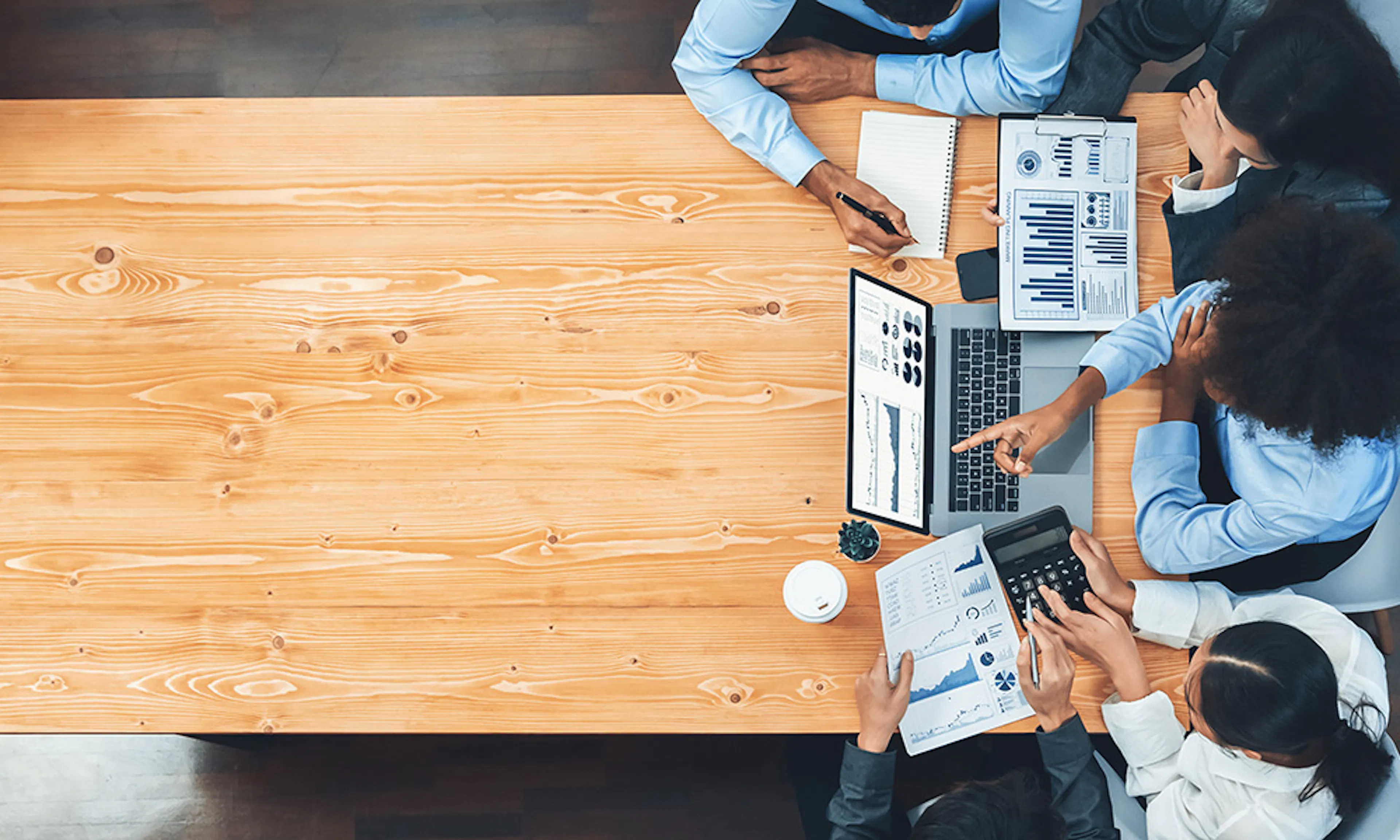 Aerial view of a table with people discussing charts and graphs at the right-hand end of the table