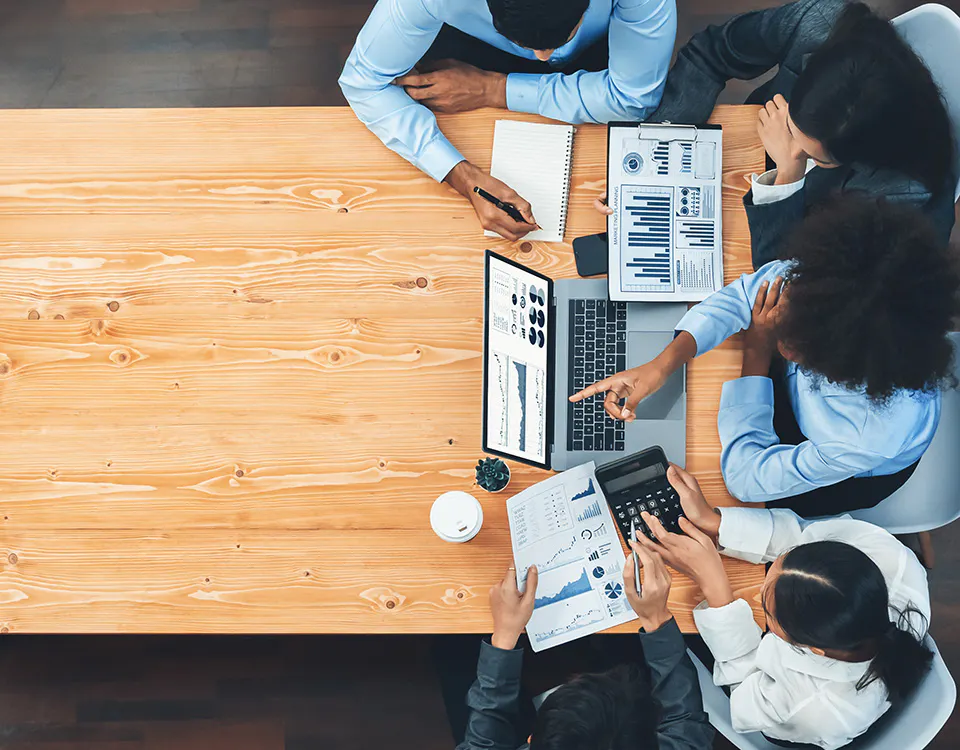 Aerial view of a table with people discussing charts and graphs at the right-hand end of the table