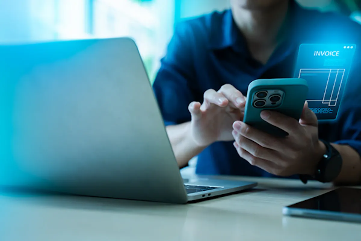 Person working with a laptop, using their phone to process an invoice