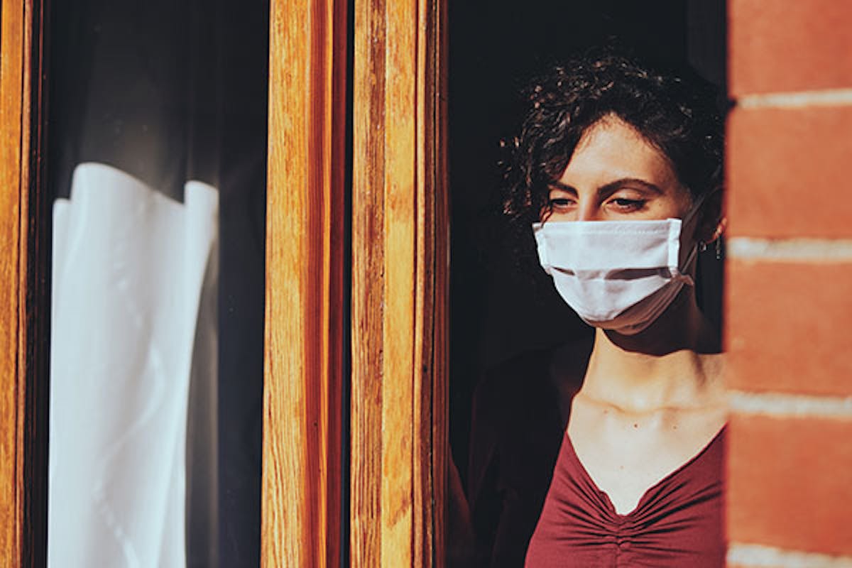 Woman standing at a window wearing a face mask