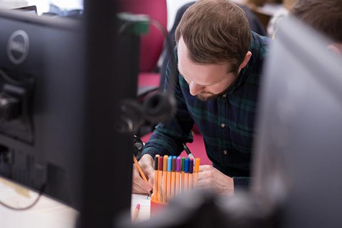 Man at a desk drawing designs with coloured pens