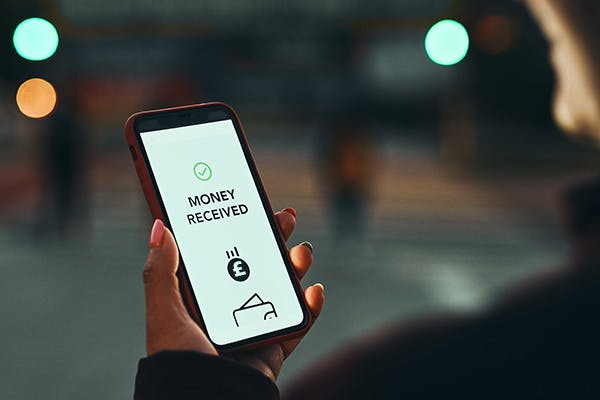 Hand holding a mobile phone with the display reading Money Received