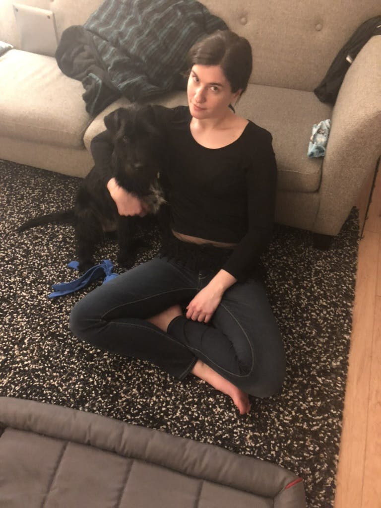 A woman puts her arm around a black scruffy dog