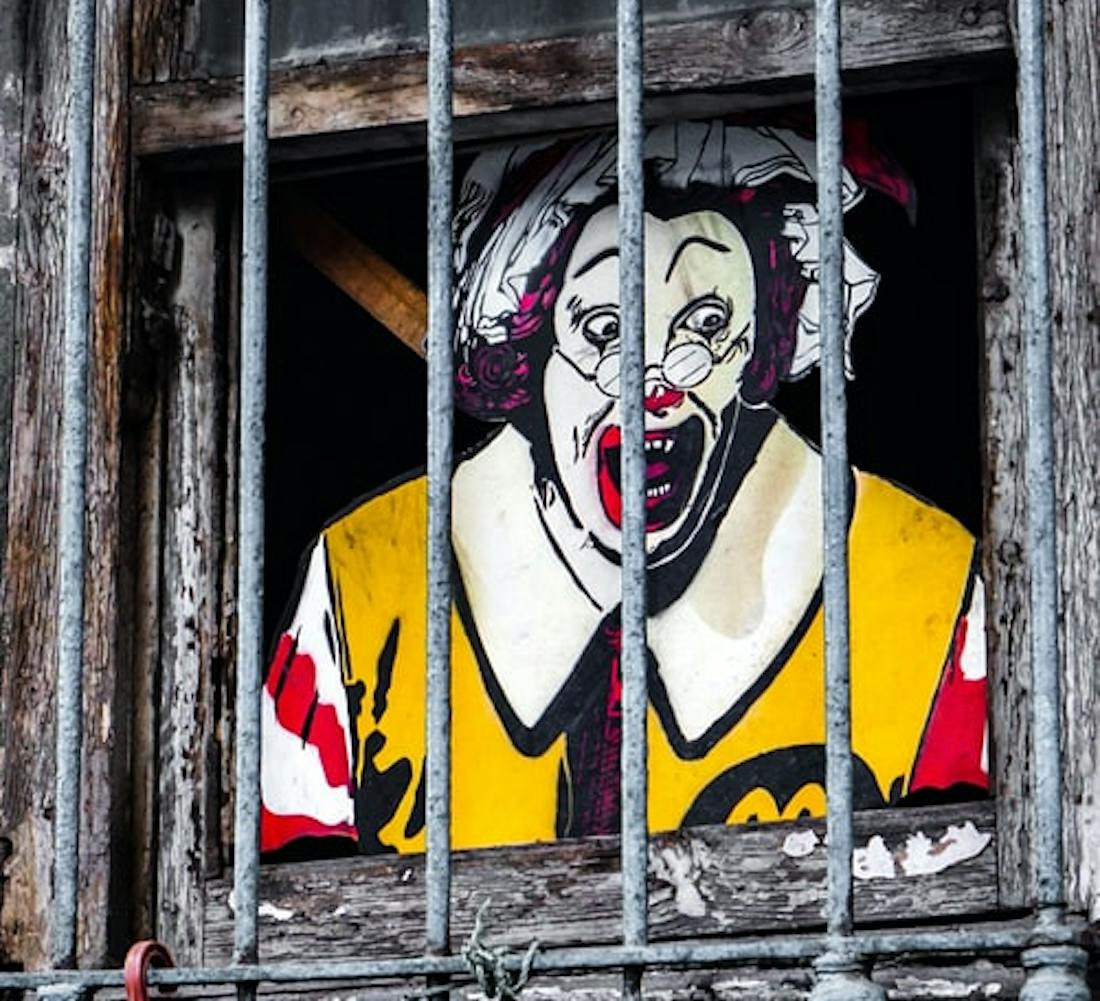 Ronald McDonald screaming behind bars in a wooden frame