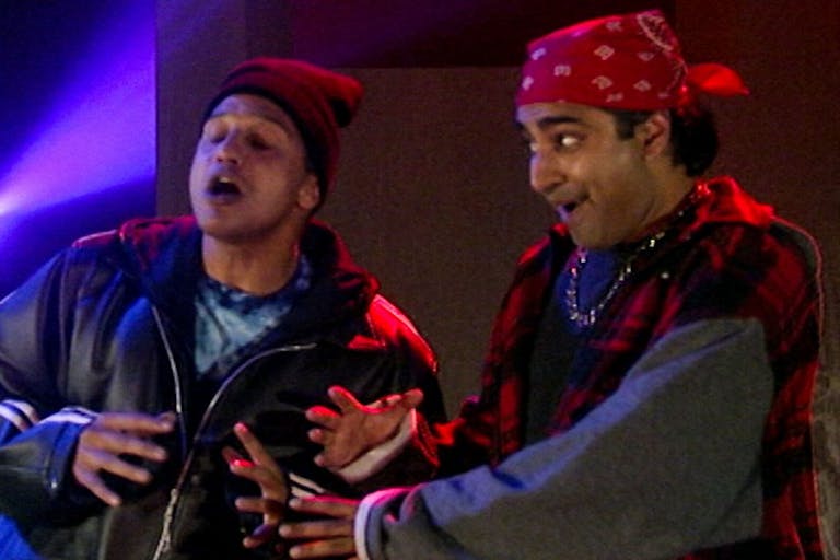 Two Asian men dressed as young fans of hip hop, wearing a beanie and bandana and chains, rapping and being animated