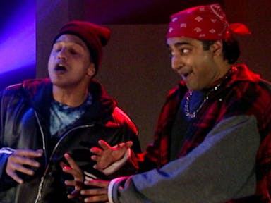 Two Asian men dressed as young fans of hip hop, wearing a beanie and bandana and chains, rapping and being animated