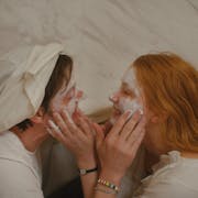 Man and woman hold each others faces in the bathroom, smiling and putting cream on each other