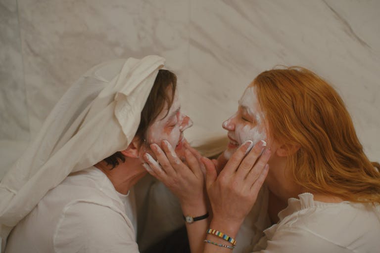 Man and woman hold each others faces in the bathroom, smiling and putting cream on each other