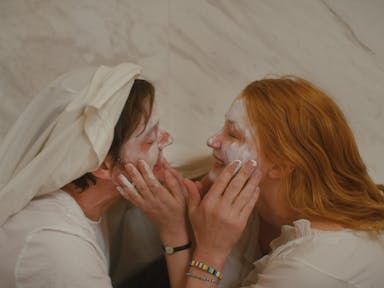 Man and woman hold each others faces in the bathroom, smiling and putting cream on each other