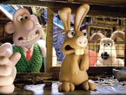 Stop motion animation of a white man with wide mouth putting his hand in a rabbit hutch gingerly towards a shaking brown rabbit; a light brown dog stands upright looking through the wire hutch window