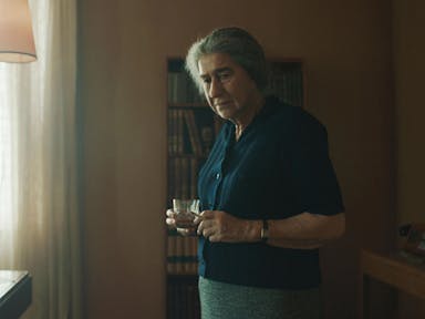 Older woman in an office holds a cup of tea